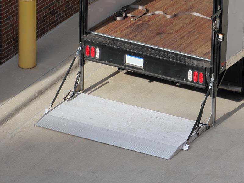 Small white moving and hauling truck with a lift on the back sits in a loading dock area. The back of the truck is open and cargo are is visible and empty.